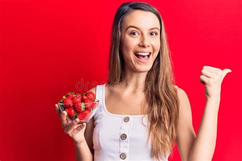 Young Beautiful Girl Holding Bowl With Strawberries Pointing Thumb Up