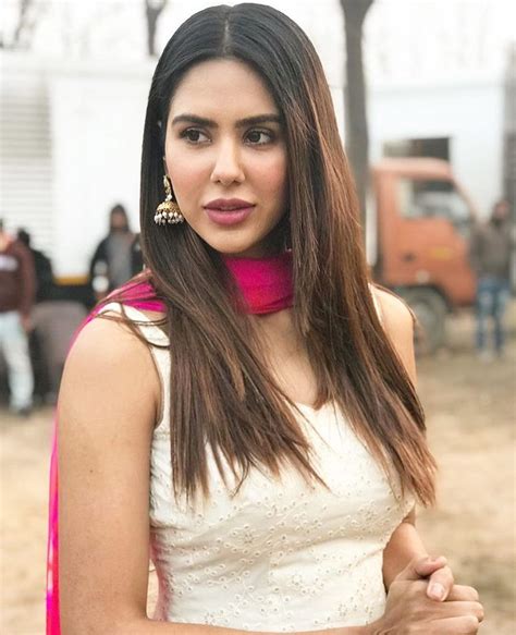 a woman with long brown hair wearing a white dress and pink scarf on her neck