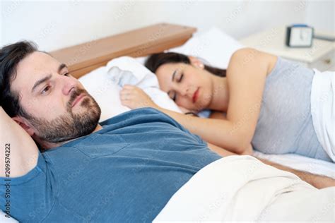 Upset Man Having Problem Lying In The Bed With His Sleeping Girlfriend