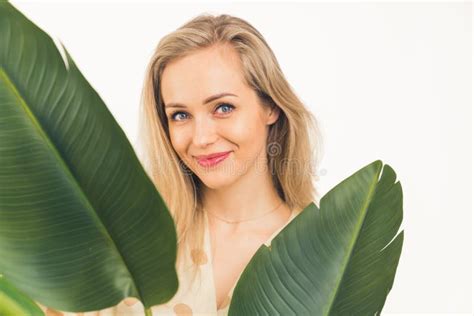 attractive caucasian blue eyed blonde girl behind the green leaves smiling and looking into the