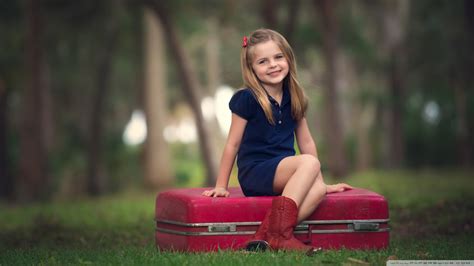 Smiley Cute Little Girl Is Wearing Blue Dress Sitting On Red Suitcase