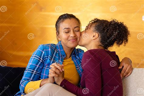 Happy Biracial Lesbian Couple Embracing And Kissing On Sofa In Living Room Stock Image Image