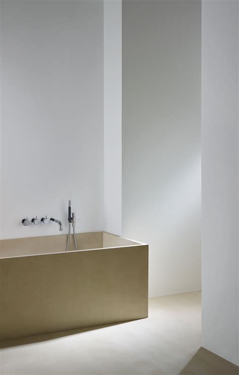 A Bathtub In A White Bathroom Next To A Wall With Two Faucets