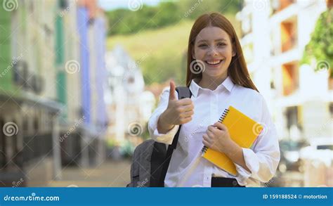Happy Female High Schooler With Rucksack And Books Gesturing Thumbs Up