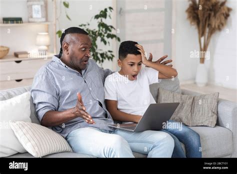 Black Man And His Grandson Looking At Laptop Screen With Shock Stock