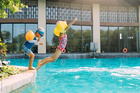 Two Kids Jumping Into Swimming Pool Del Colaborador De Stocksy