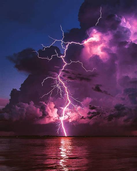 A Purple And Blue Sky With Lightning Striking Over The Ocean