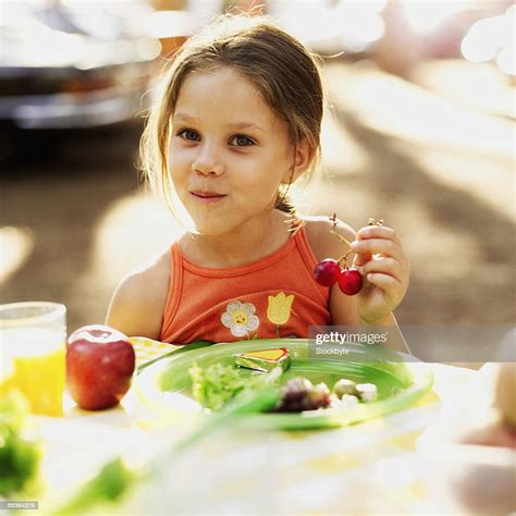Portrait Of A Girl Sitting At A Picnic Table Holding Cherries High Res