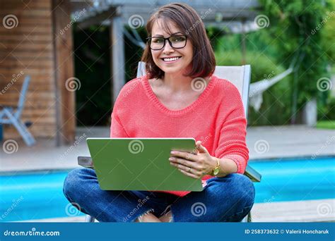 Middle Aged Woman Sitting In Chair In Backyard With Laptop Stock Photo