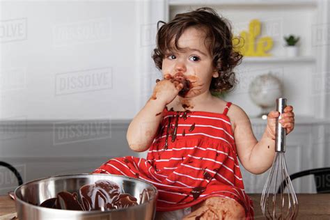 Messy Baby Girl Eating Chocolate While Sitting On Table Against Wall At