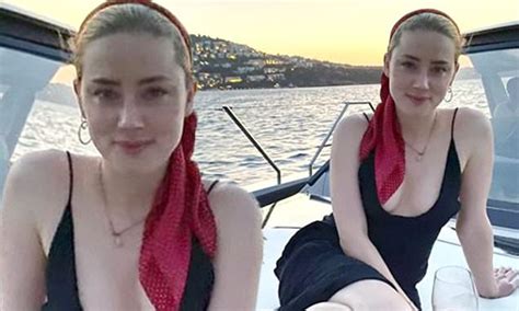 Amber Heard poses in a plunging black dress while drinking red wine on