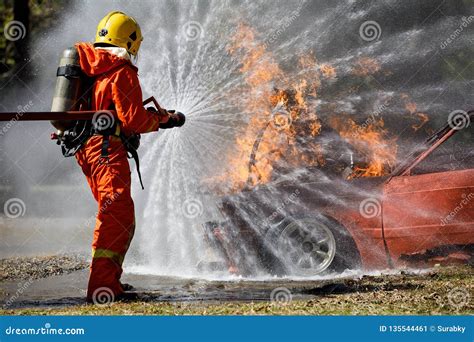 Fire Fighter Hosing Water To Extinguish A Fire Over The Car In Accident