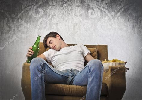 Young Man Sleeping On An Armchair While Holding A Beer Bottle And A