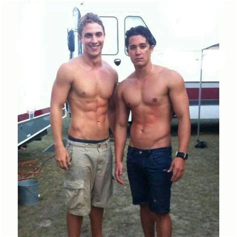 Two Men Standing Next To Each Other In Front Of A Camper Trailer With No Shirts On