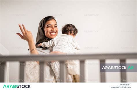 أم عربية خليجية سعودية محجبة، تحمل طفلها الرضيع بحب وحنان، إيماءات تدل على السعادة والأمان
