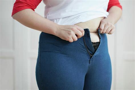 woman trying to button jeans over tummy photograph by science photo library