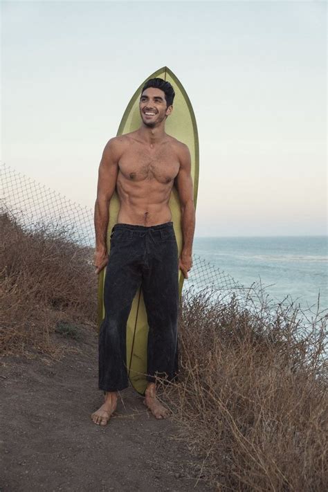 A Shirtless Man Holding A Surfboard On Top Of A Hill Near The Ocean