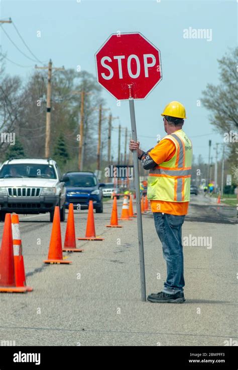 Road Worker Holds Stop Sign To Direct Traffic While A Crew Repairs A