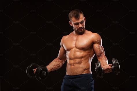 Handsome Athletic Man In Gym Is Pumping Up Muscles With Dumbbells In A