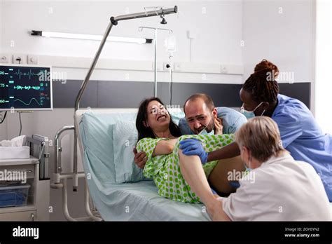 pregnant person in labor with contractions giving birth while laying in hospital ward bed at