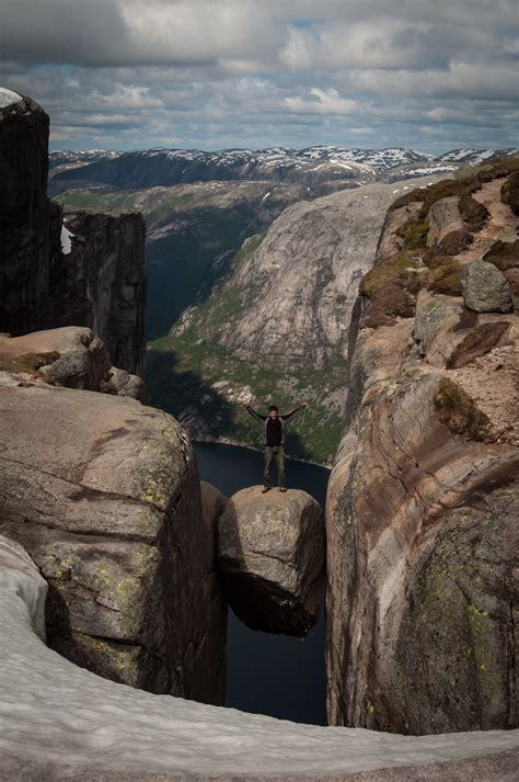 Stand On A Boulder Wedged Between Mountains At Kjeragbolten In Norway