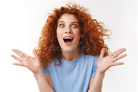 close up shot emotive attractive redhead curly haired woman raising hands up surprised and