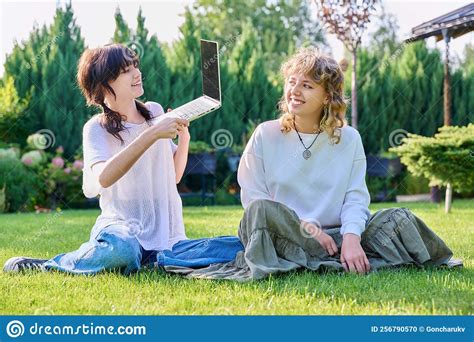 Teenage Female Student Friends Laughing Sitting On Grass With Laptop