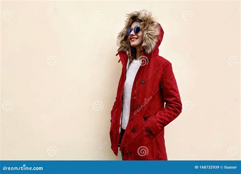 Side View Of Stylish Smiling Woman In Red Jacket With Fur Hood Standing