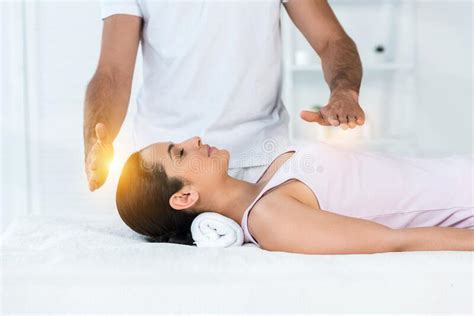 View Of Healer Putting Hands Above Body Of Attractive Woman With Closed Eyes Lying On Massage