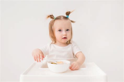 Premium Photo Baby Girl Sitting In A High Chair Eating Porridge