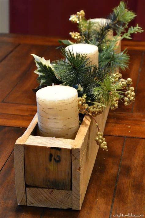 Two Candles Are Sitting In A Wooden Box With Greenery And Pine Cones On Top