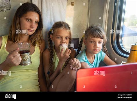 mamá y dos niñas están mirando a la pantalla del portátil en el tren coche tomando un bocado