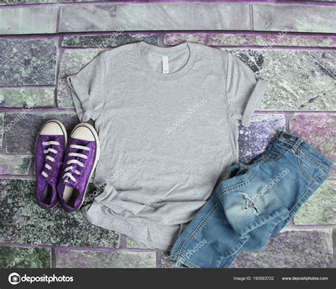 Mockup of a baby onesie on a plain color background. Gray T Shirt mockup flat lay on purple brick background ...