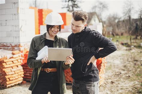 Stylish Woman Architect With Tablet And Foreman Checking Blueprints At