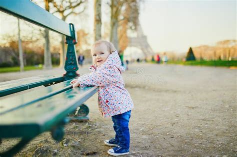 One Year Old Girl Standing Next To Bench Near The Eiffel Tower Stock