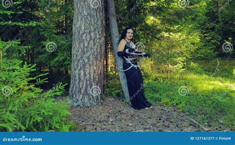 A Woman Of A Witch In Black Clothes In A Forest Is Tied With Chains To