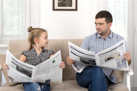 jeune fille avec son père assis sur le sofa à la maison et en lisant le journal ensemble la même