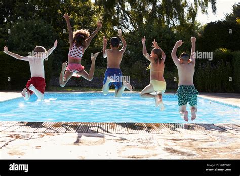 Rear View Of Children Jumping Into Outdoor Swimming Pool Stock Photo