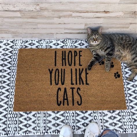 A Cat Sitting On Top Of A Door Mat That Says I Hope You Like Cats