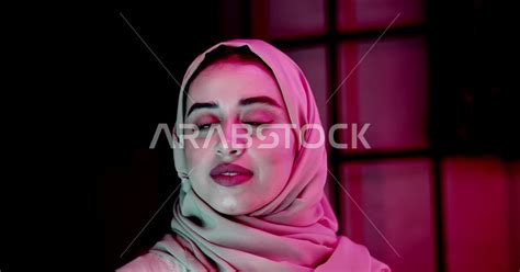 إمرأة عربية سعودية خليجية محجبة، تقوم بجلسة تصوير مع إضاءة ملونة، مبتسمة تنظر إلى الكاميرا