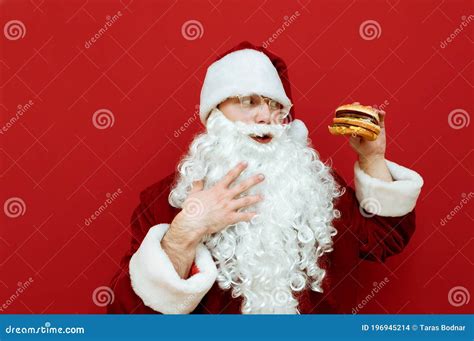 Portrait Of Hungry Santa Claus Looking At Burger In Hand And Stroking