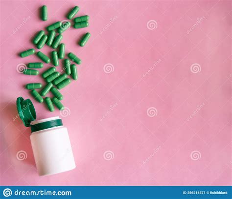 medication bottle and green pills spilled on pink pastel coloured background medication and