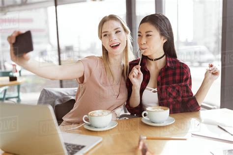 Smiling Young Women Taking Selfie While Drinking Coffee Indoors At