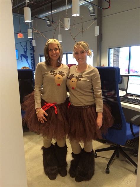Two Women Standing Next To Each Other In Front Of A Computer Desk Wearing Reindeer Costumes