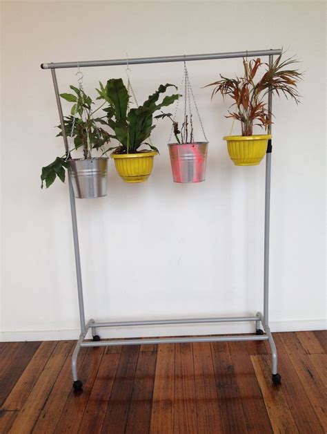 Three Potted Plants Sitting On Top Of A Metal Rack Next To A White Wall