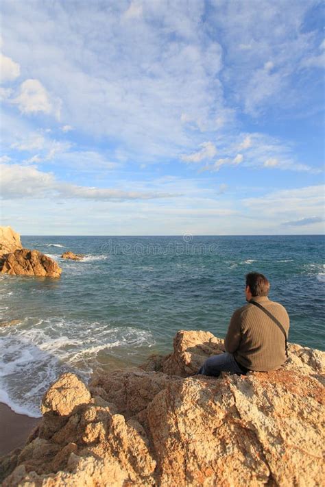 Man Sitting On A Rock In The Beach And Looking The Sea Stock Image