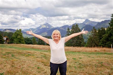 Emotional Elderly Woman Stands Among Mountains With Outstretched Arms
