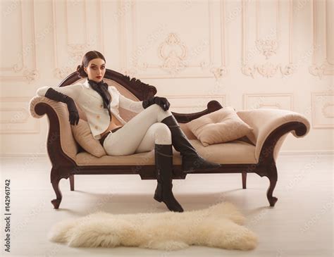 strict beautiful girl in elegant rider suit poses on camera restrained interior vintage sofa