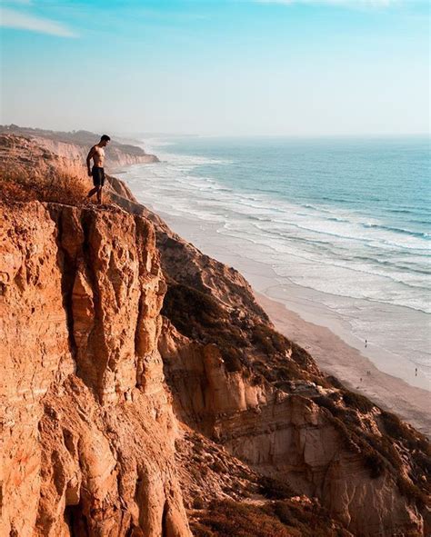 A Man Standing On Top Of A Cliff Next To The Ocean