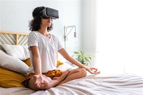 Latina Woman Meditating With Help Of Vr Experience App Sitting On Bed